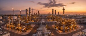 Luftaufnahme einer Raffinerie bei Sonnenuntergang mit zahlreichen Rohrleitungen, Türmen, Lagerbehältern und Fackeln.